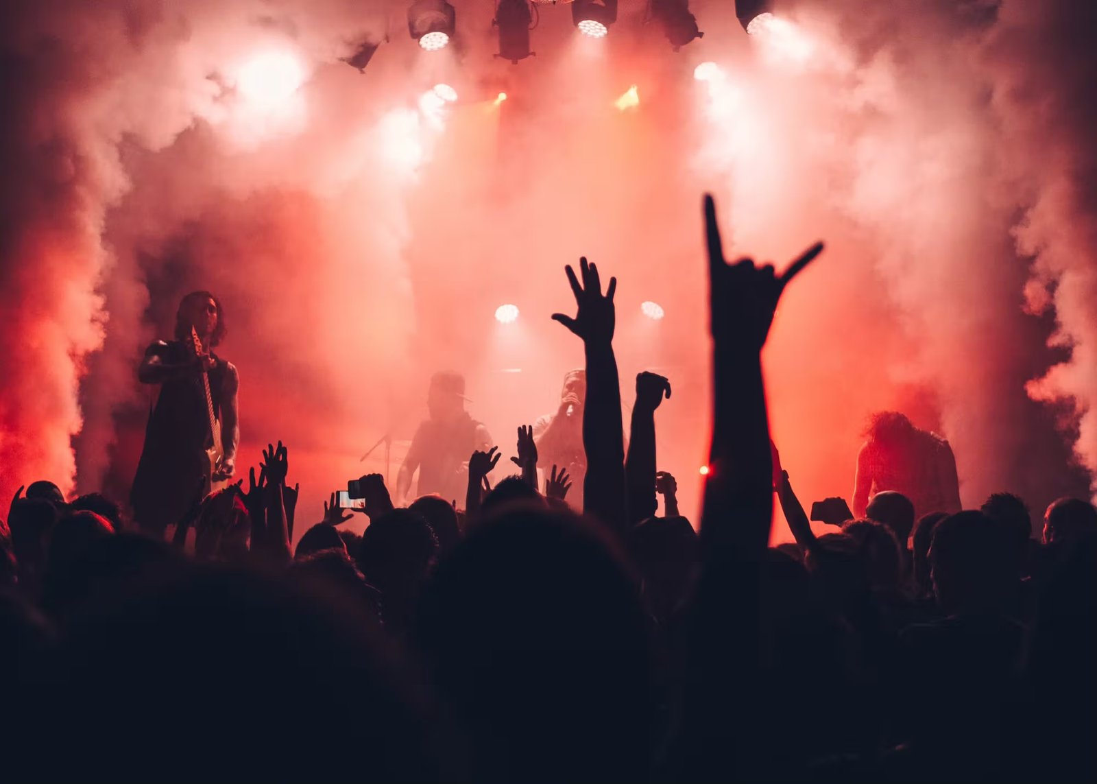 A crowd throwing hands up under red stage haze.